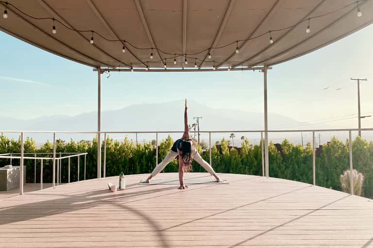 Woman doing yoga on wooden deck under retractable shade with mountain views in background