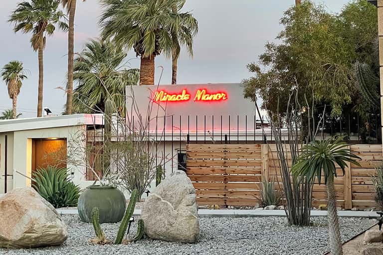 Neon 'Miracle Manor' sign on mid-century modern building with palm trees