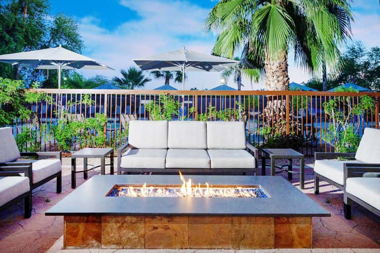 Lakeside patio with fire pit, upholstered seating, umbrellas, and palm tree landscaping