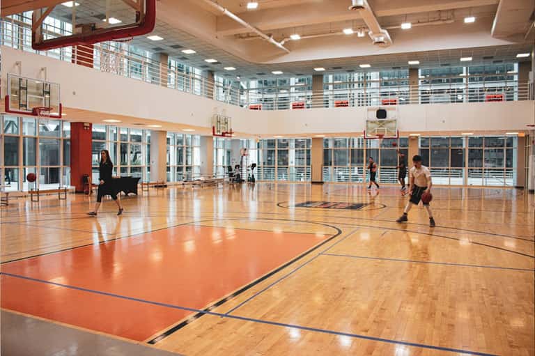 Bright indoor gymnasium with wooden flooring, basketball hoops, and large windows