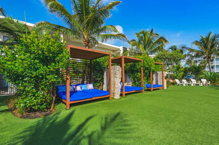 Orange and teal canopy daybed on manicured lawn with palm trees and resort buildings