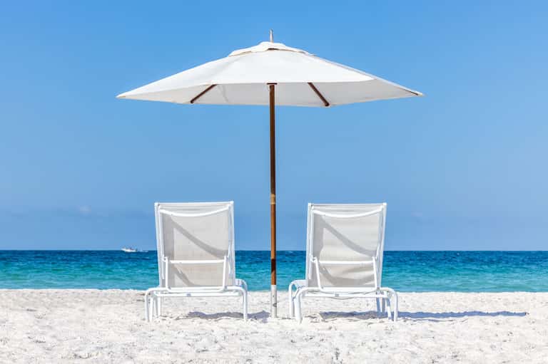 Two white lounge chairs under a white umbrella on a sandy beach with turquoise ocean