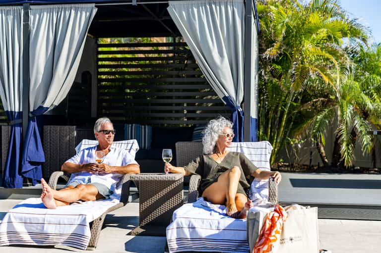 Couple relaxing on lounge chairs under cabana with ocean view and palm trees