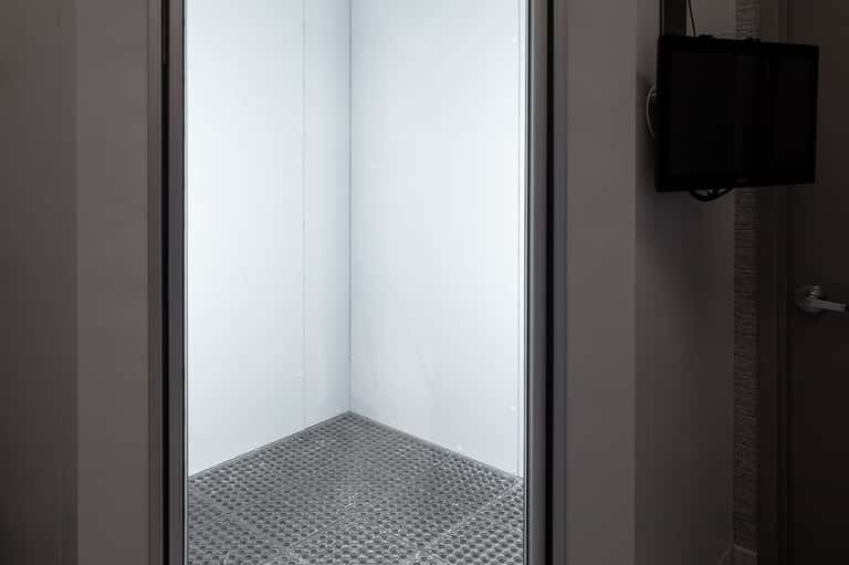 Clean, modern bathroom shower stall with white walls, glass enclosure, and textured floor mat