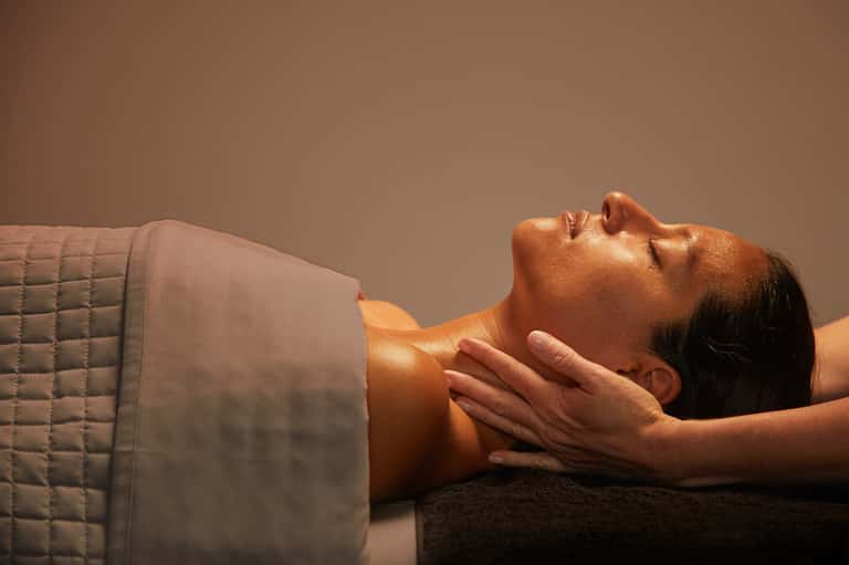 Spa therapist performing neck massage on relaxed client in warm lighting