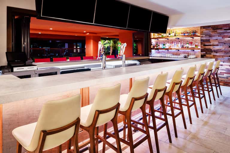 Modern bar interior with cream bar stools, orange accent walls, and well-stocked liquor shelves