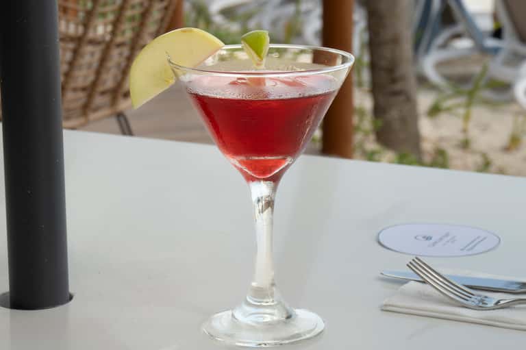 Red cocktail with lime garnish on white table at beachfront dining venue