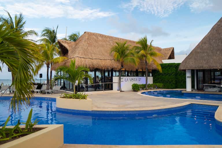 Tropical resort with thatched-roof bungalows, palm trees, and multiple blue pools