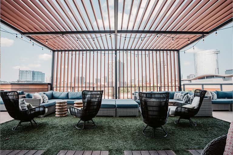 Modern rooftop lounge with retractable shade, blue seating, and city skyline views