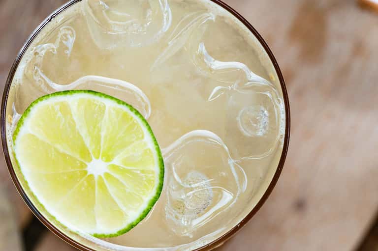 Refreshing cocktail with lime slice and ice in a clear glass on wooden surface
