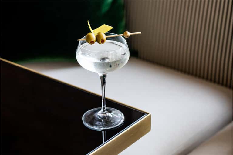 Cocktail glass with olives and lemon garnish on a bar counter
