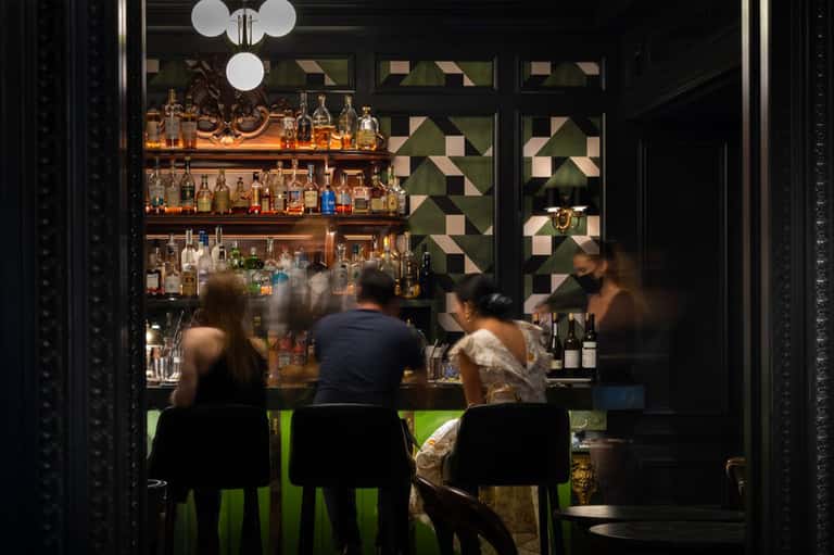 Upscale bar interior with illuminated shelving, geometric wall patterns, and seated patrons