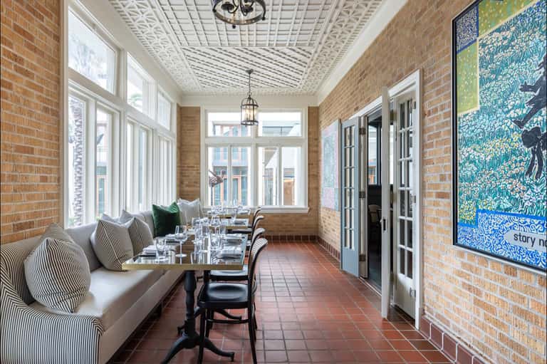 Elegant dining room with exposed brick walls, ornate ceiling, banquette seating, and decorative artwork