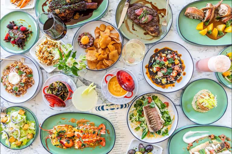 Overhead view of shared dining table with colorful plates of gourmet dishes, meats, seafood, and appetizers