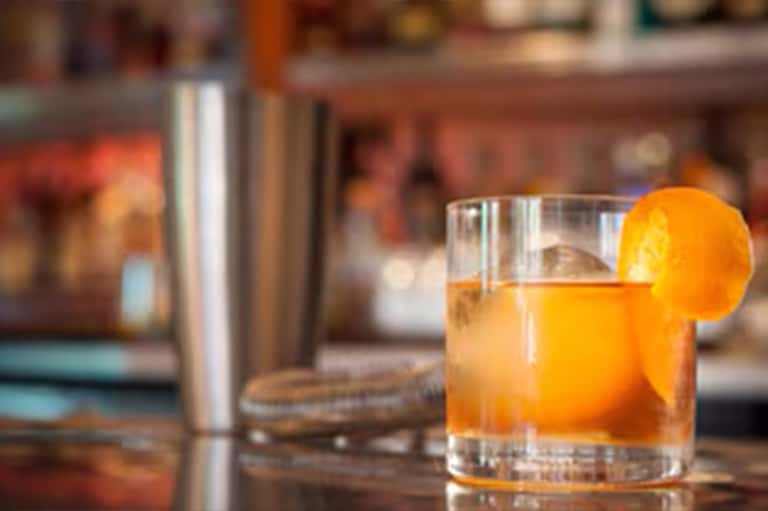 Cocktail with orange slice garnish and metal shaker on bar counter
