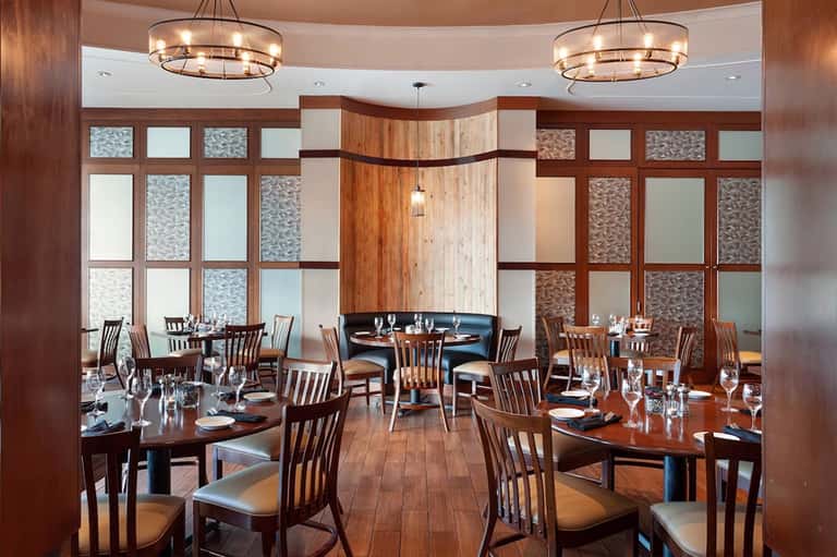 Upscale dining room with wooden tables, chairs, pendant lights, and grid-patterned windows