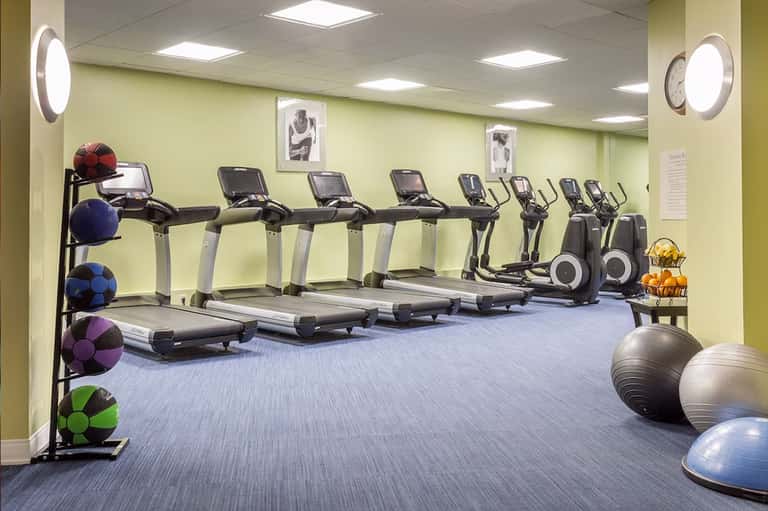 Modern gym with treadmills, ellipticals, exercise balls, and bright yellow-green walls