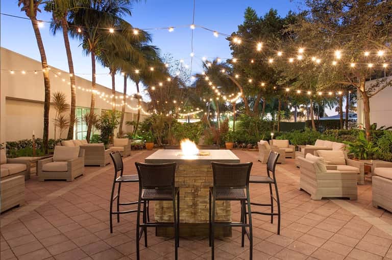 Outdoor courtyard at dusk with firepit, lounge seating, string lights, and palm trees