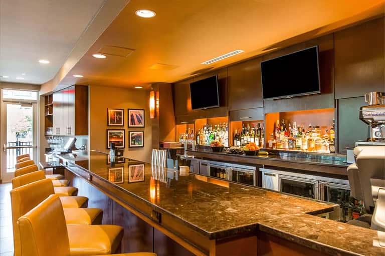 Upscale bar interior with orange ceiling, dark wood, and full liquor display