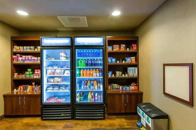 Hotel snack bar with refrigerated beverage cases, shelving with packaged goods, and wooden cabinetry