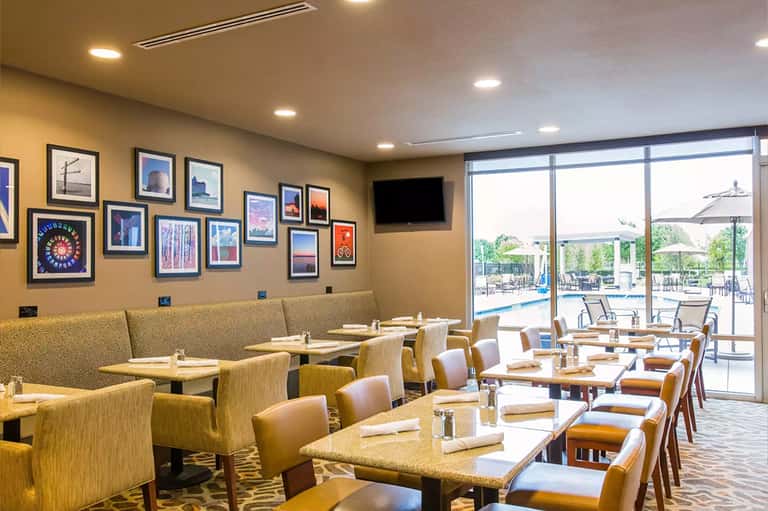Bright dining area with gold upholstered seating, framed artwork on mustard walls, and ocean view through glass doors