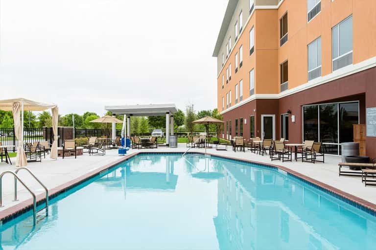 Resort outdoor pool with lounge chairs, pergola shade structures, and brick hotel building