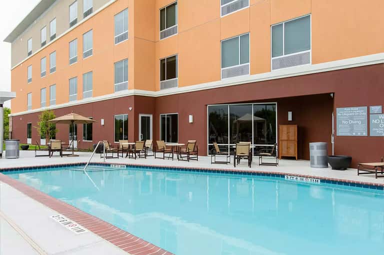 Hotel outdoor pool with tan umbrellas, loungers, and orange building with brown trim