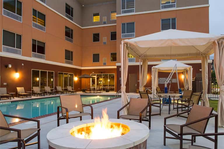 Resort pool deck at dusk with fire pit, lounge chairs, cabanas, and illuminated building