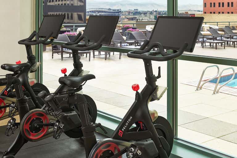 Fitness center with stationary bikes overlooking urban skyline and outdoor pool area through large windows