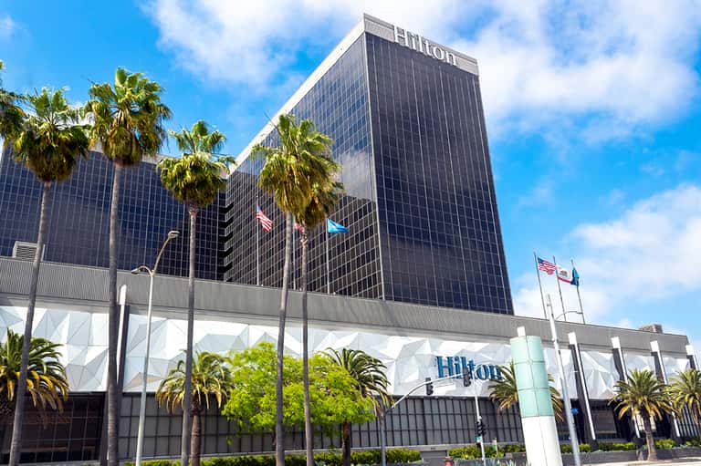 Hilton hotel exterior with dark facade, palm trees, and white entry canopy with flags