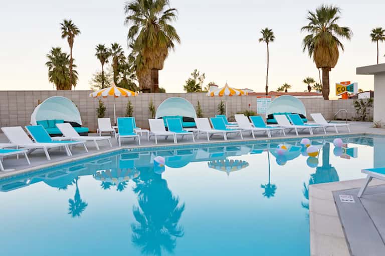 Resort pool with turquoise water, cabanas, lounge chairs, and palm trees under clear sky
