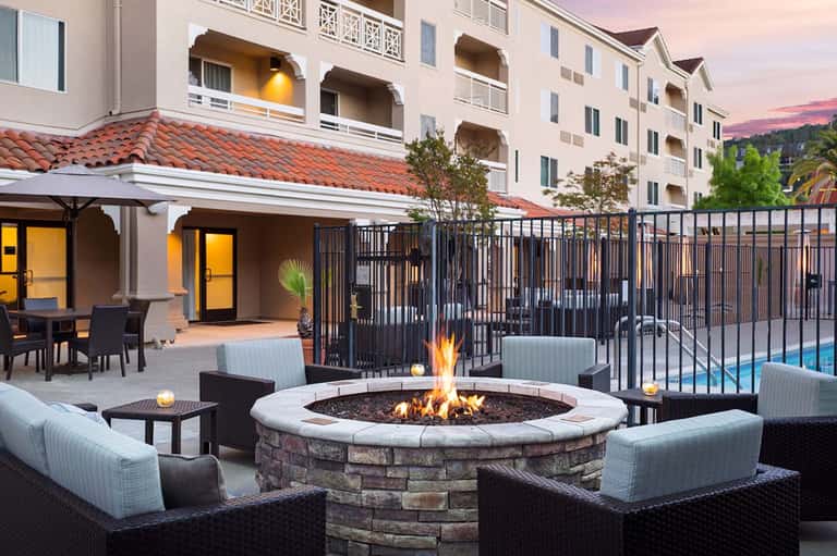 Outdoor fire pit seating area with fireplace, lounge chairs, and resort buildings at dusk