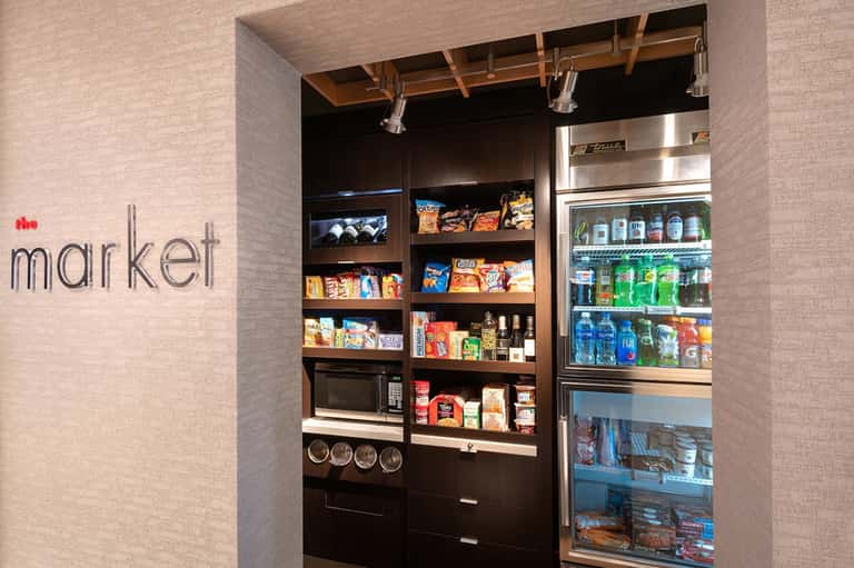 Modern hotel market convenience station with dark wooden shelves displaying snacks, beverages, and microwave
