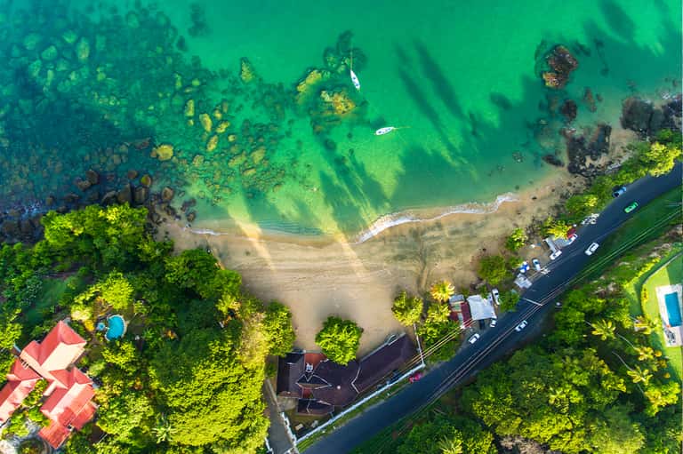 Aerial view of pristine beach cove surrounded by lush green forest with turquoise water