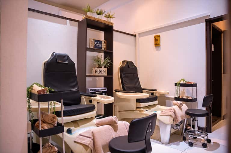 Spa pedicure station with black leather chairs, footbaths, and decorative plants in a pink and beige room