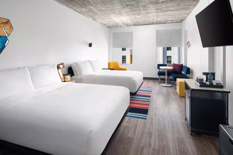 Modern hotel room with two queen beds, white bedding, flat-screen TV, and minimalist décor