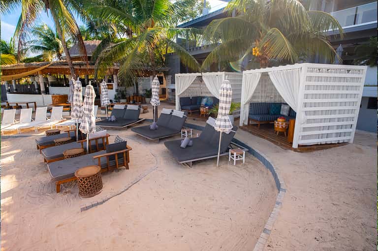 Beach club with white cabana tents, black lounge chairs, and palm trees