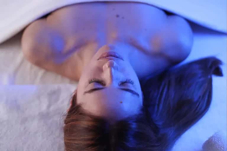 Woman relaxing on bed with blue ambient lighting and white linens