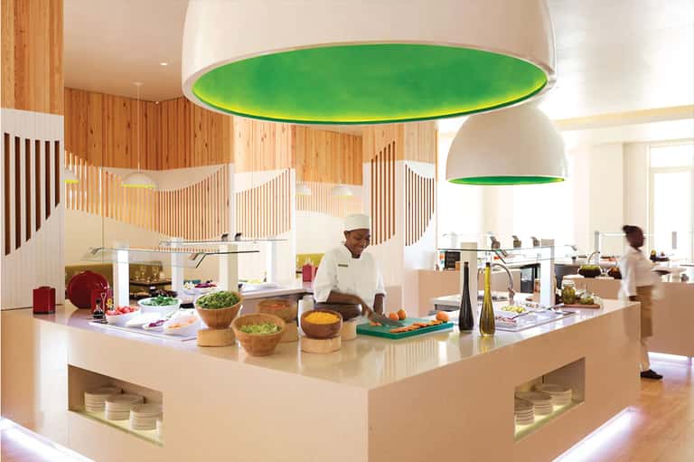 Modern open kitchen with chef preparing food under green pendant lights