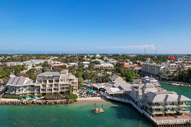 Aerial view of beachfront resort with white buildings, pools, and waterfront docks