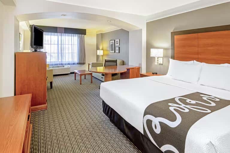 Hotel room with queen bed, wood furnishings, TV, desk, and lounge seating area