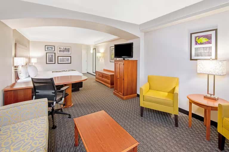 Spacious hotel suite with king bed, yellow accent chair, wood furniture, and curved ceiling details