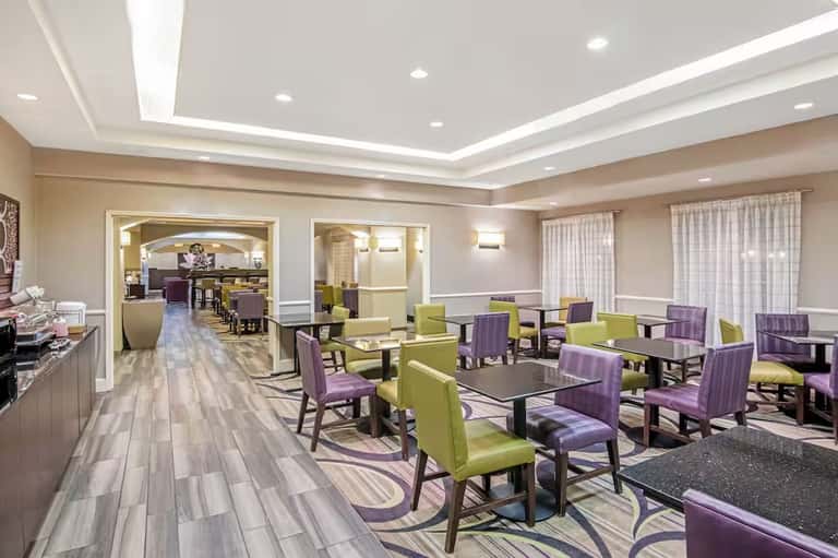 Spacious hotel lounge with purple and green upholstered chairs, coffered ceiling, and neutral tones