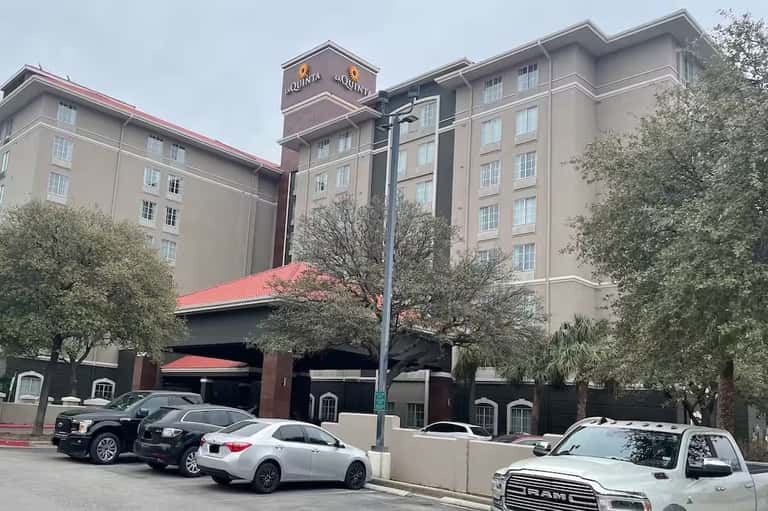 La Quinta hotel exterior with tan multi-story building, red roof accents, and parking lot with vehicles