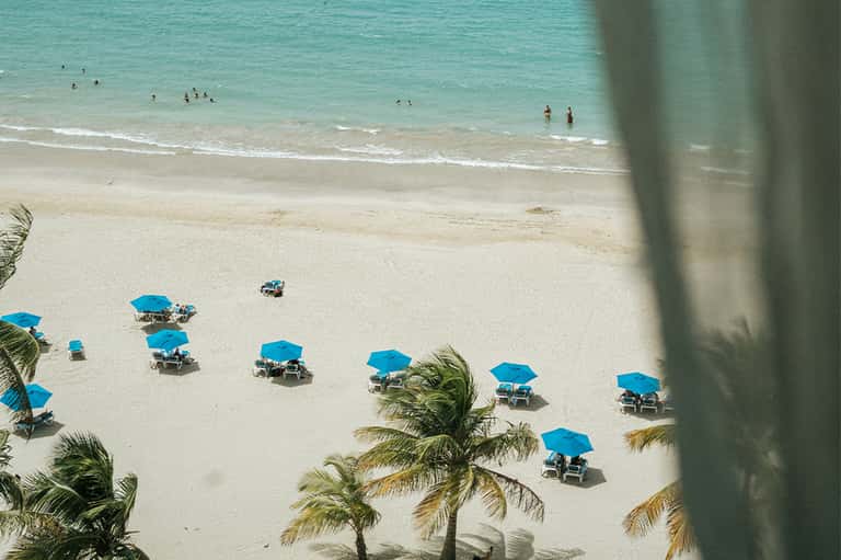 Aerial view of sandy beach with turquoise water and blue umbrellas near palm trees
