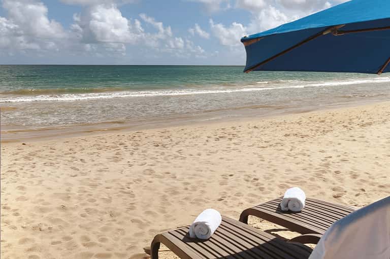 Beach scene with lounge chairs, rolled towels, blue boat, and calm turquoise water