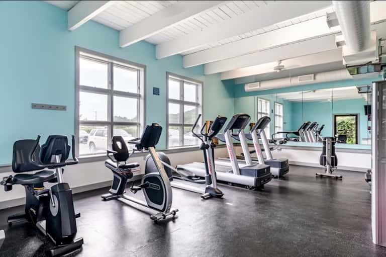 Bright turquoise fitness center with exercise bikes, treadmills, large windows, and mirrored walls
