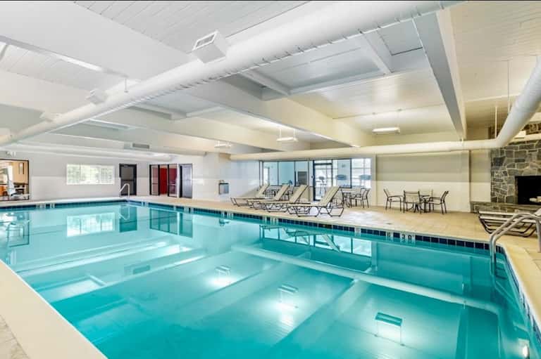 Indoor swimming pool with high ceilings, lounge chairs, and stone fireplace