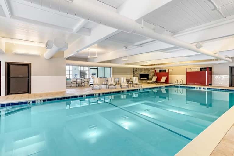 Indoor Olympic-size swimming pool with lap lanes, white ceiling beams, and lounge seating area