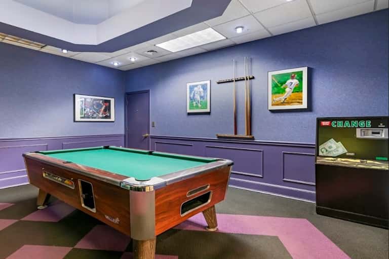 Recreation room with pool table, purple walls, sports artwork, and billiards equipment